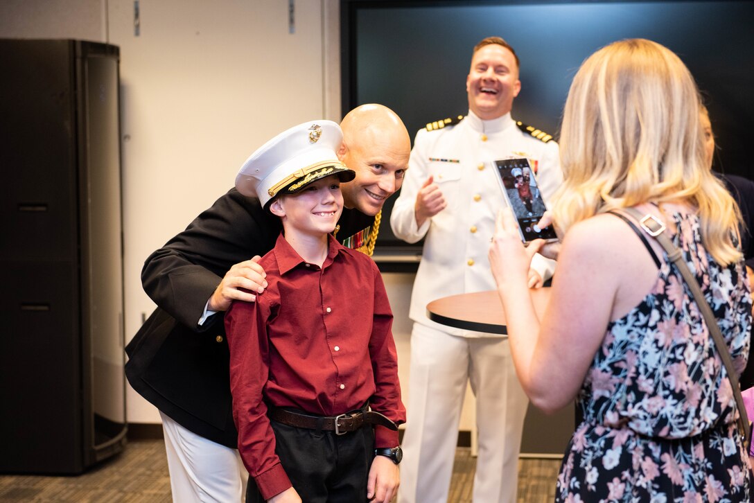 The son of Marine Corps Maj. Kyle Huston pose for a picture as his son wears Dad's hat at a reception after the Defense Logistics Agency Land and Maritime Change of Command and Retirement Ceremony July 22. Huston is pictured behind his son and his wife is taking the photo.