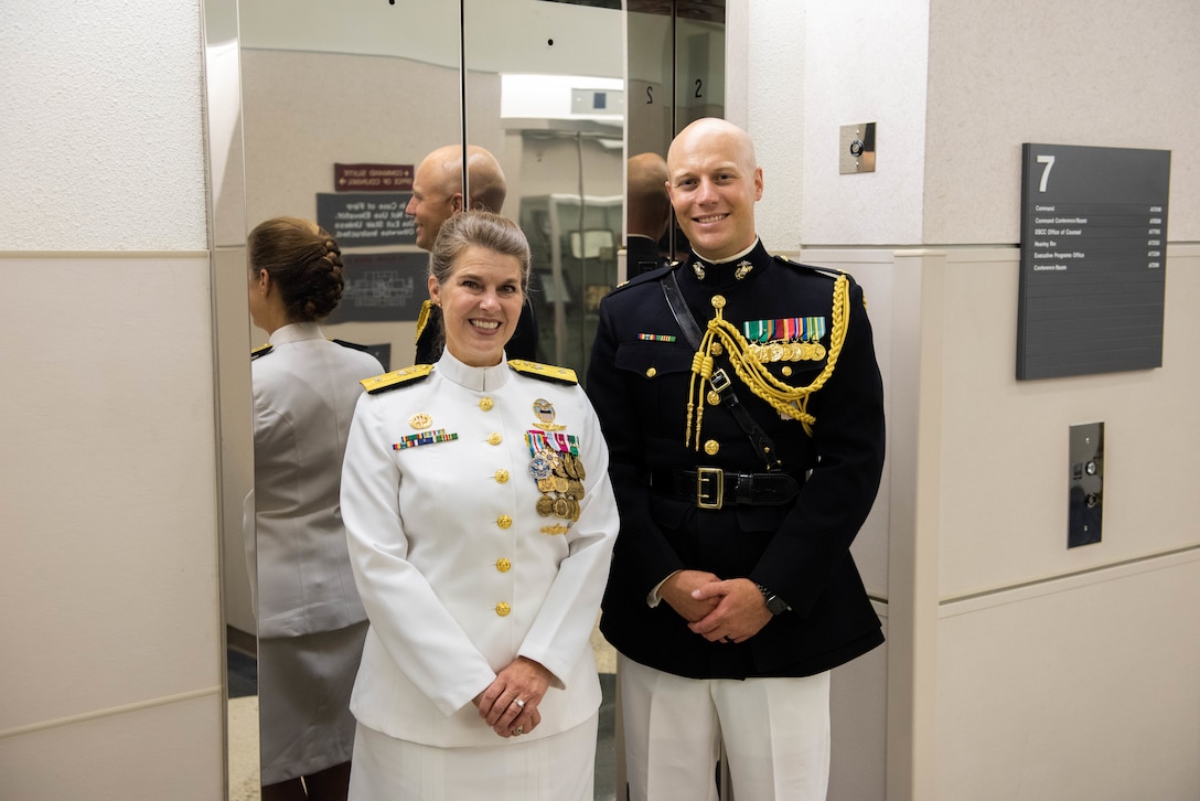 A man in a black and gold Marine Corps uniform with a woman in a pure white Navy uniform with gold trim smile at the camera.