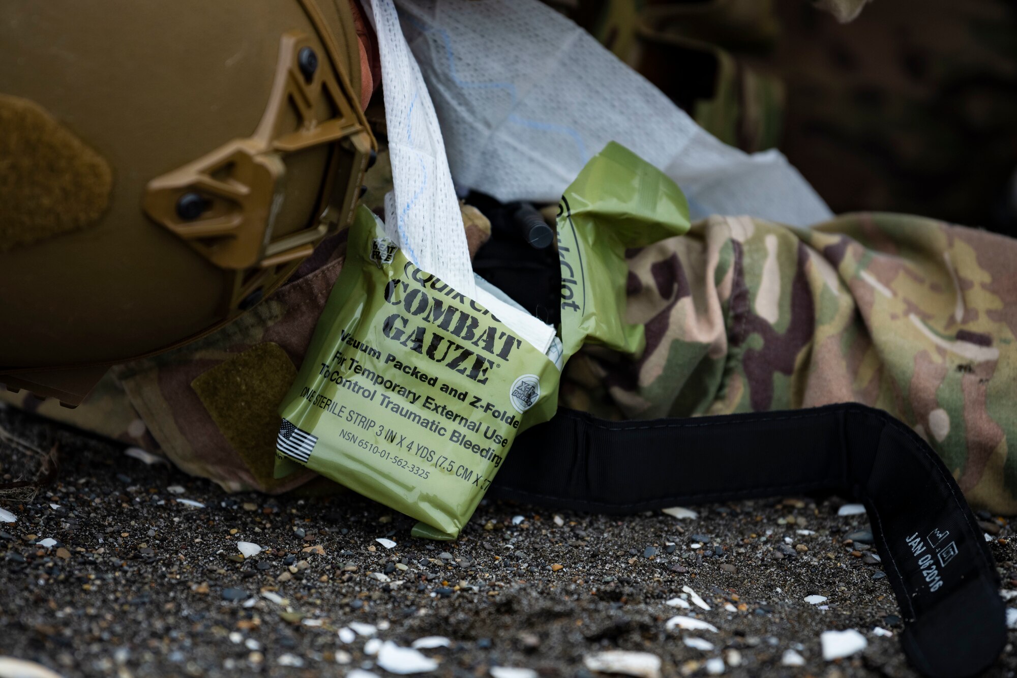 A package of combat gauze lays on the ground while being applied to a U.S. military member in tactical gear.