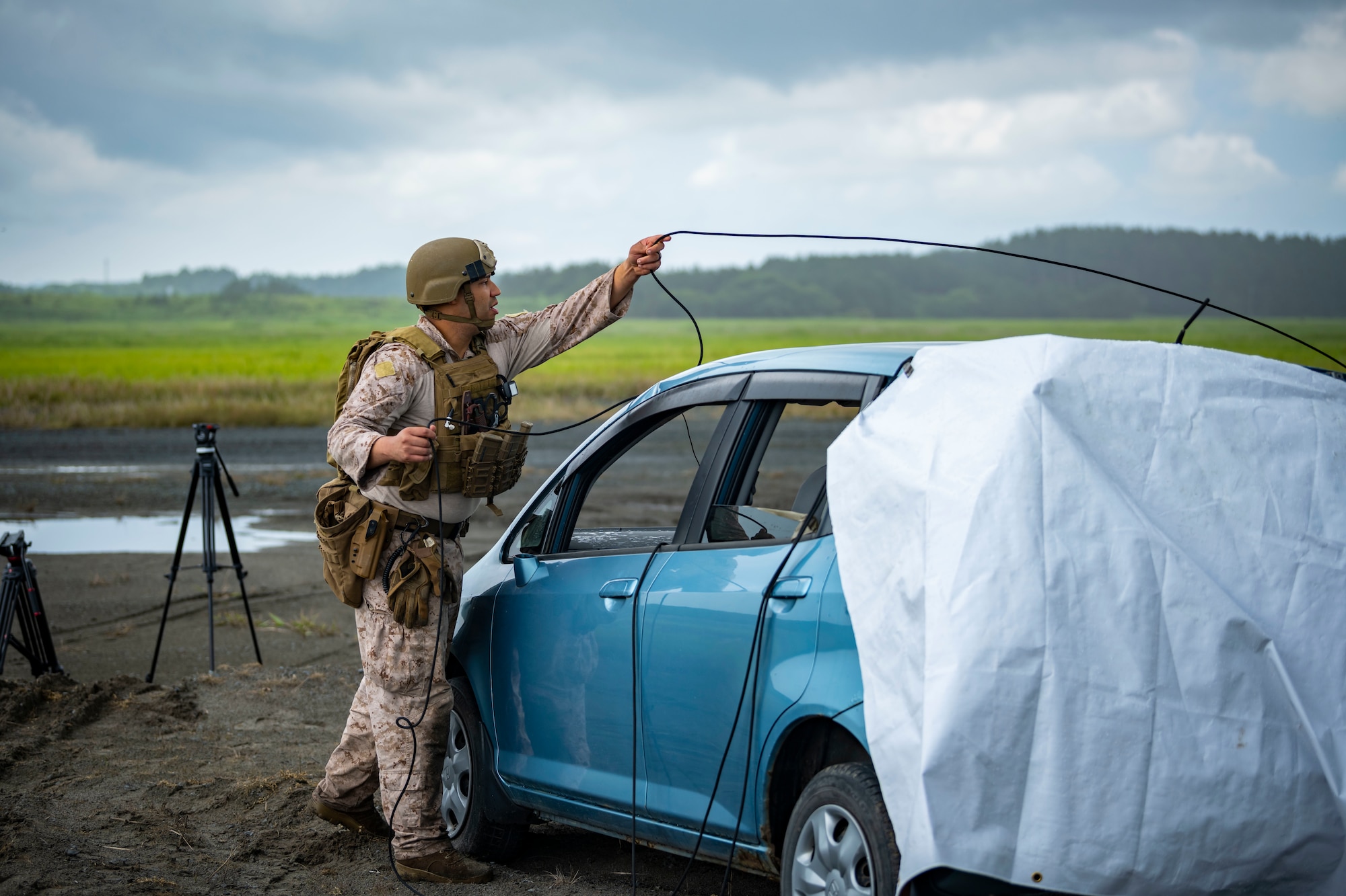 U.S. military member in tactical gear wraps cables around a car to open the door.