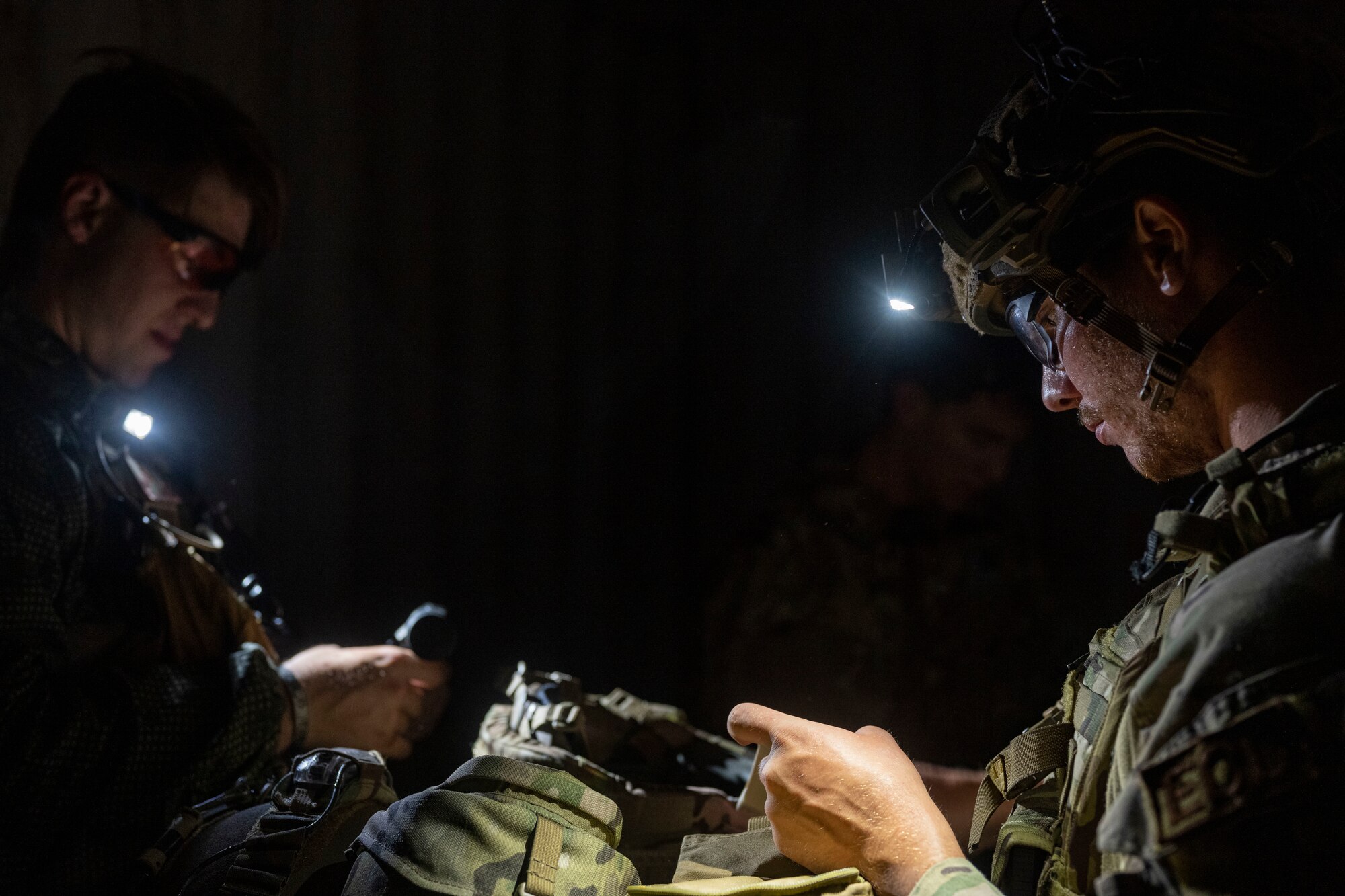 U.S. military members in tactical gear put away equipment in a containter.