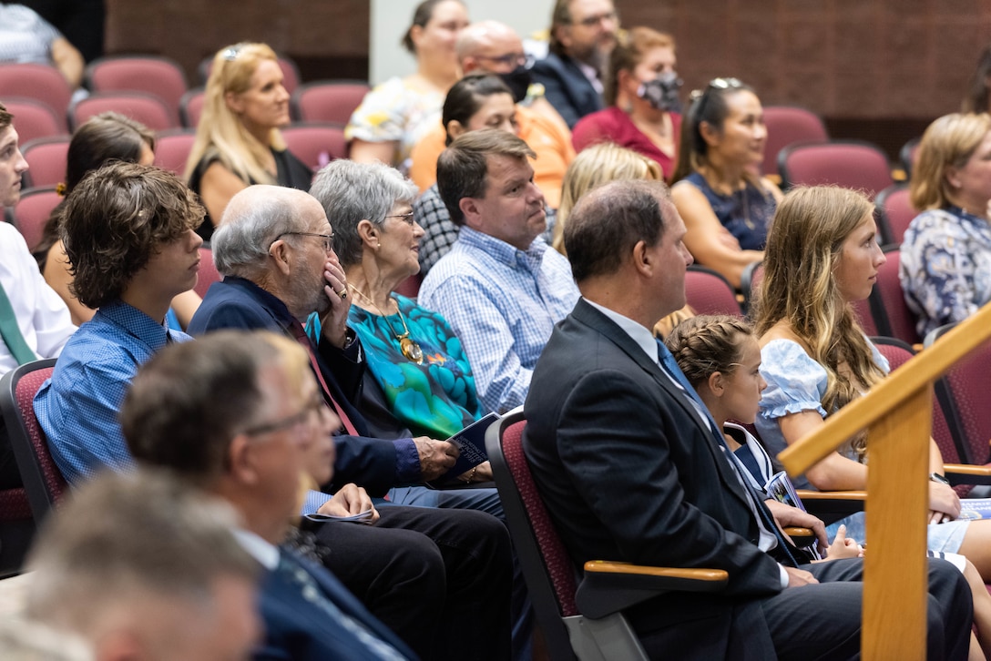 A large group of people are seated in a auditorium. All are in dressy attire. A mix of males and females. Older people and younger people.