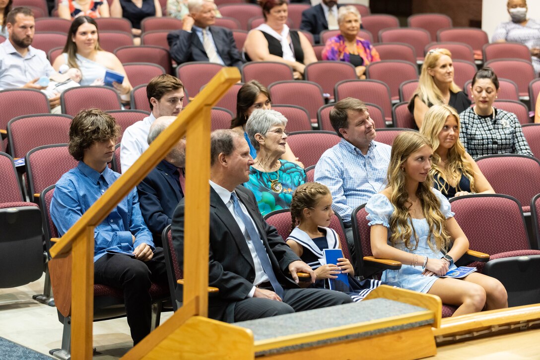 A large group of people are seated in a auditorium. All are in dressy attire. A mix of males and females. Some are in uniform and some are not.