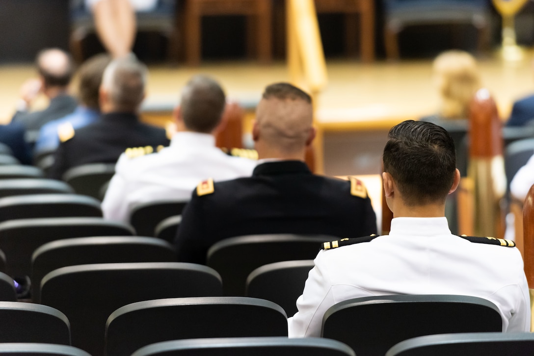 Several military members are seated in an auditorium. A mix of Navy and Army.