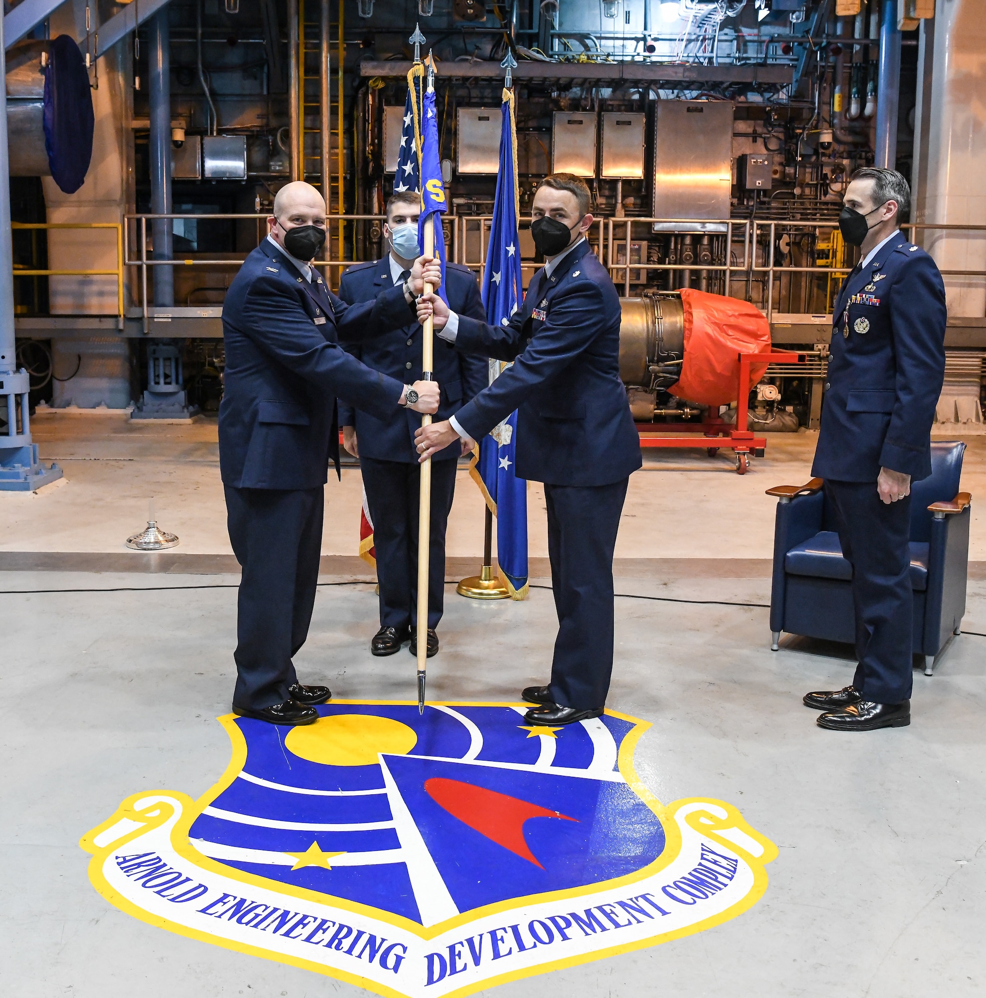Col. Jason Vap, standing at left, commander, 804th Test Group, passes the 717th Test Squadron guidon to Lt. Col. Ryne Roady, standing right, charging him with command of the squadron during a change of command ceremony July 8, 2022, in an engine test cell at Arnold Air Force Base.