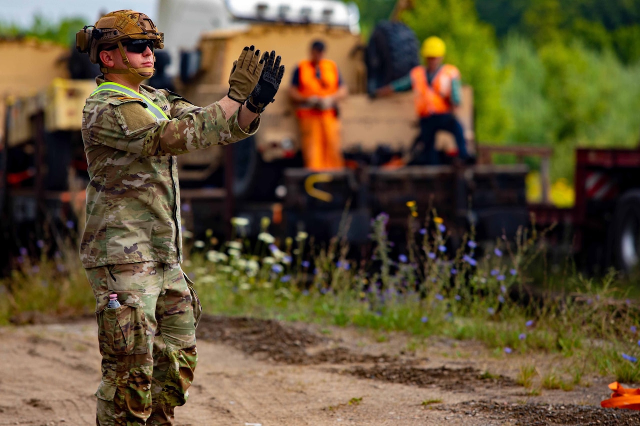 A soldier directs a vehicle using arm signals.