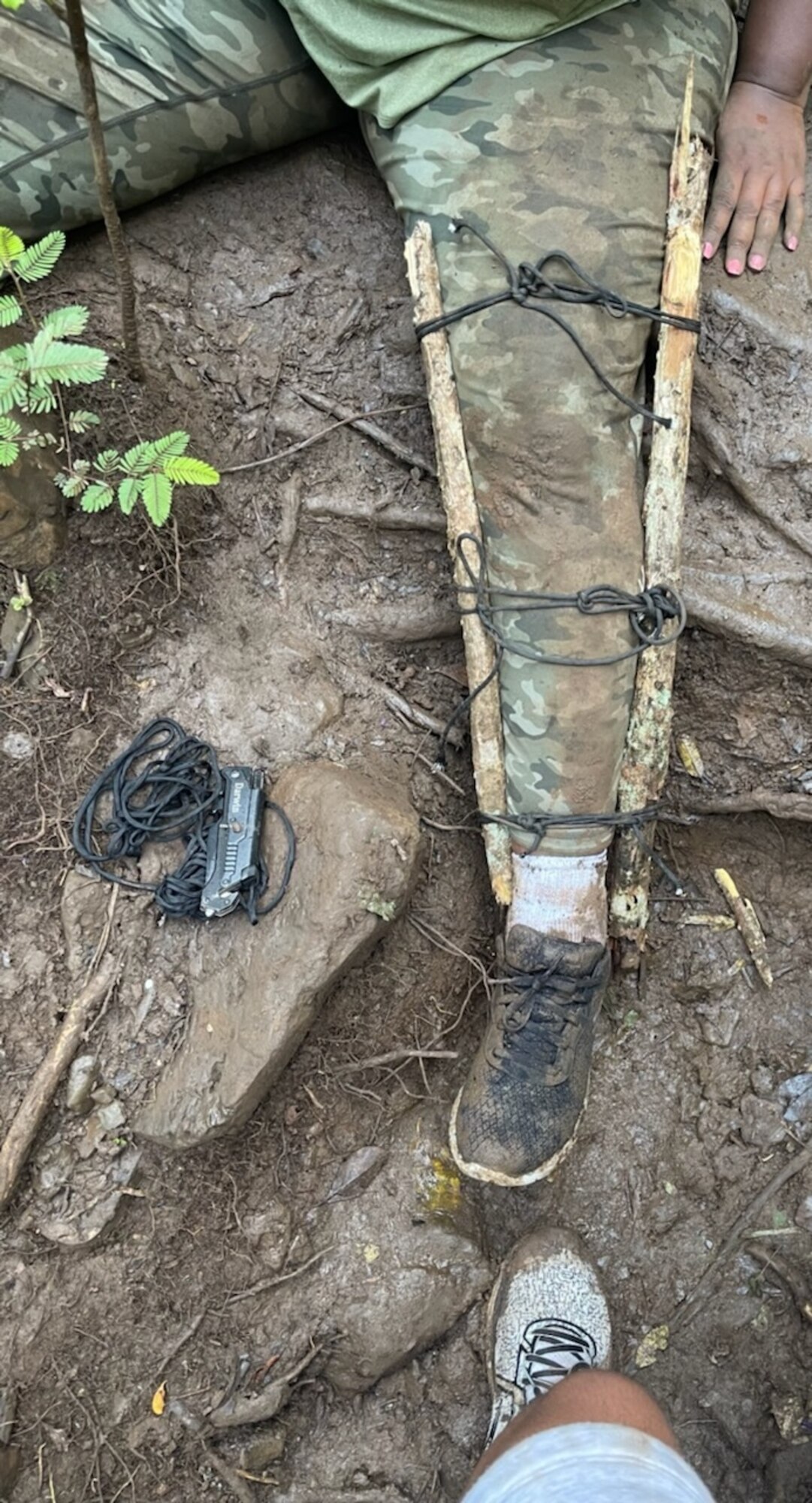 The leg of Diane Heard, 15th Wing Violence Prevention investigator, is being stabilized with a makeshift splint near Waimano Falls in Pearl City, Hawaii, July 17, 2022. One sailor and five Airmen, who stayed with Heard, made the splint from tree branches and rope in order to stabilize the injured ankle and knee. (Courtesy Photo)