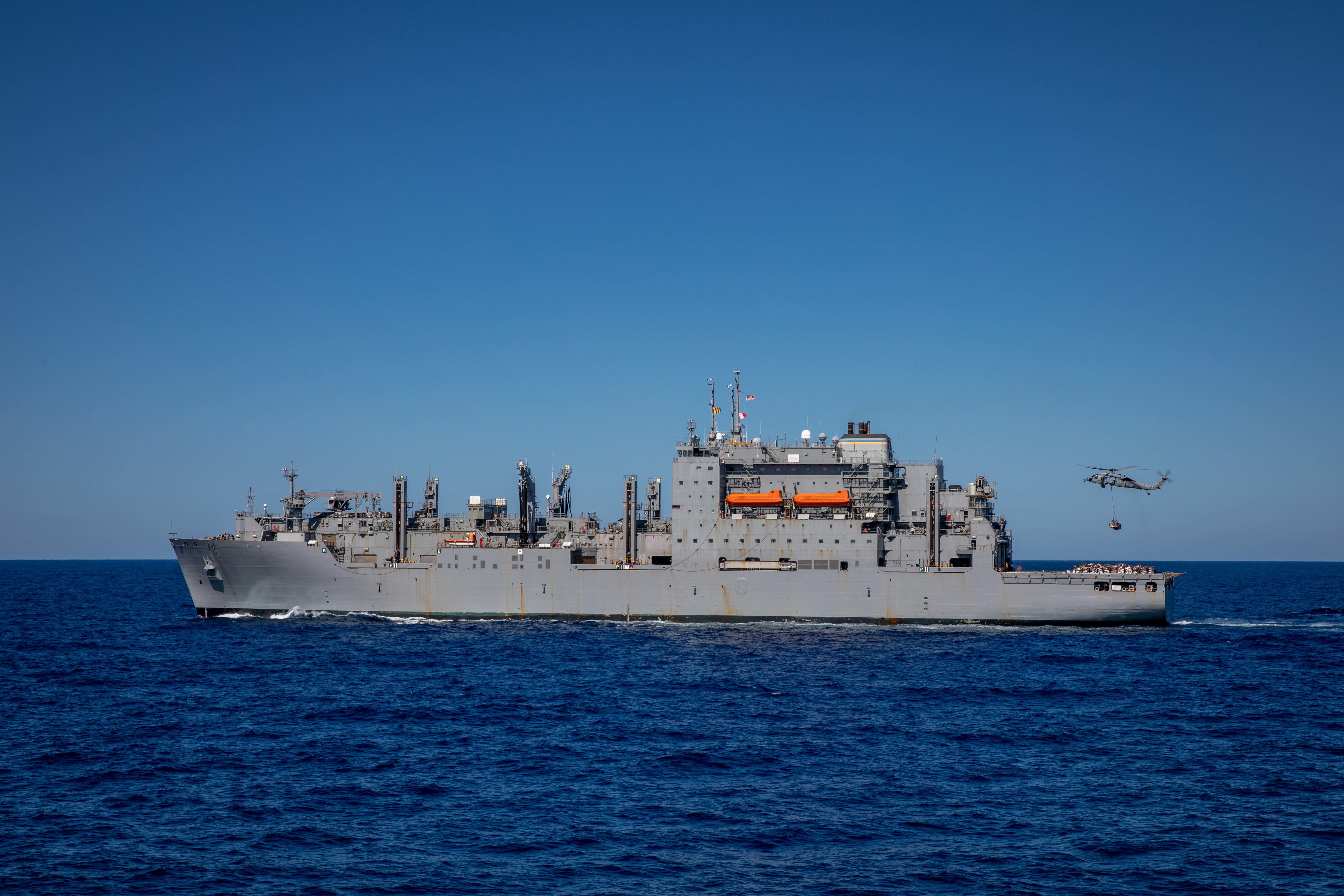 A U.S. Navy MH-60S Sea Hawk helicopter, attached to Helicopter Sea Combat Squadron (HSC) 28, deployed aboard the Wasp-class amphibious assault ship USS Kearsarge (LHD 3), retrieves cargo from the Lewis and Clark-class dry cargo ship USNS William McLean (T-AKE 12), for a vertical replenishment with the San Antonio-class amphibious transport dock ship USS Arlington (LPD 24), July 27, 2022.