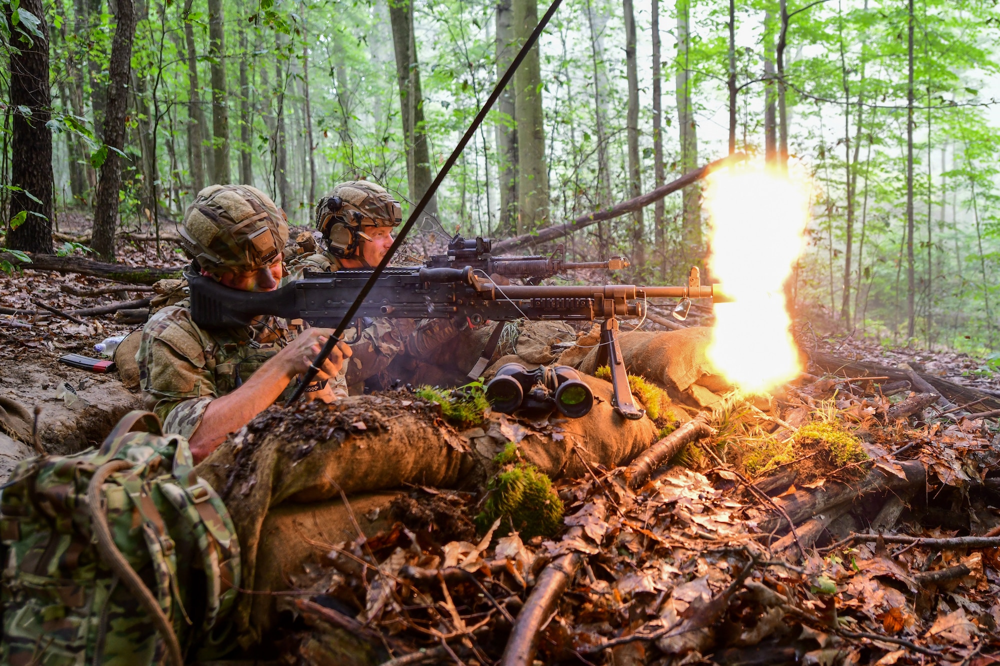 Airman 1st Class Drew Davis, Integrated Defense Leadership Course student assigned to the 307th Security Forces Squadron, Barksdale Air Force Base, Louisiana, fires blank rounds from his M240 machine gun toward opposing force members while Daniel Knight, an IDLC student assigned to the 302nd Security Forces Squadron, Peterson Space Force Base, Colorado, engages with his M4 during a static defense exercise at Camp James A. Garfield Joint Military Training Center, Ohio, July 27, 2022.