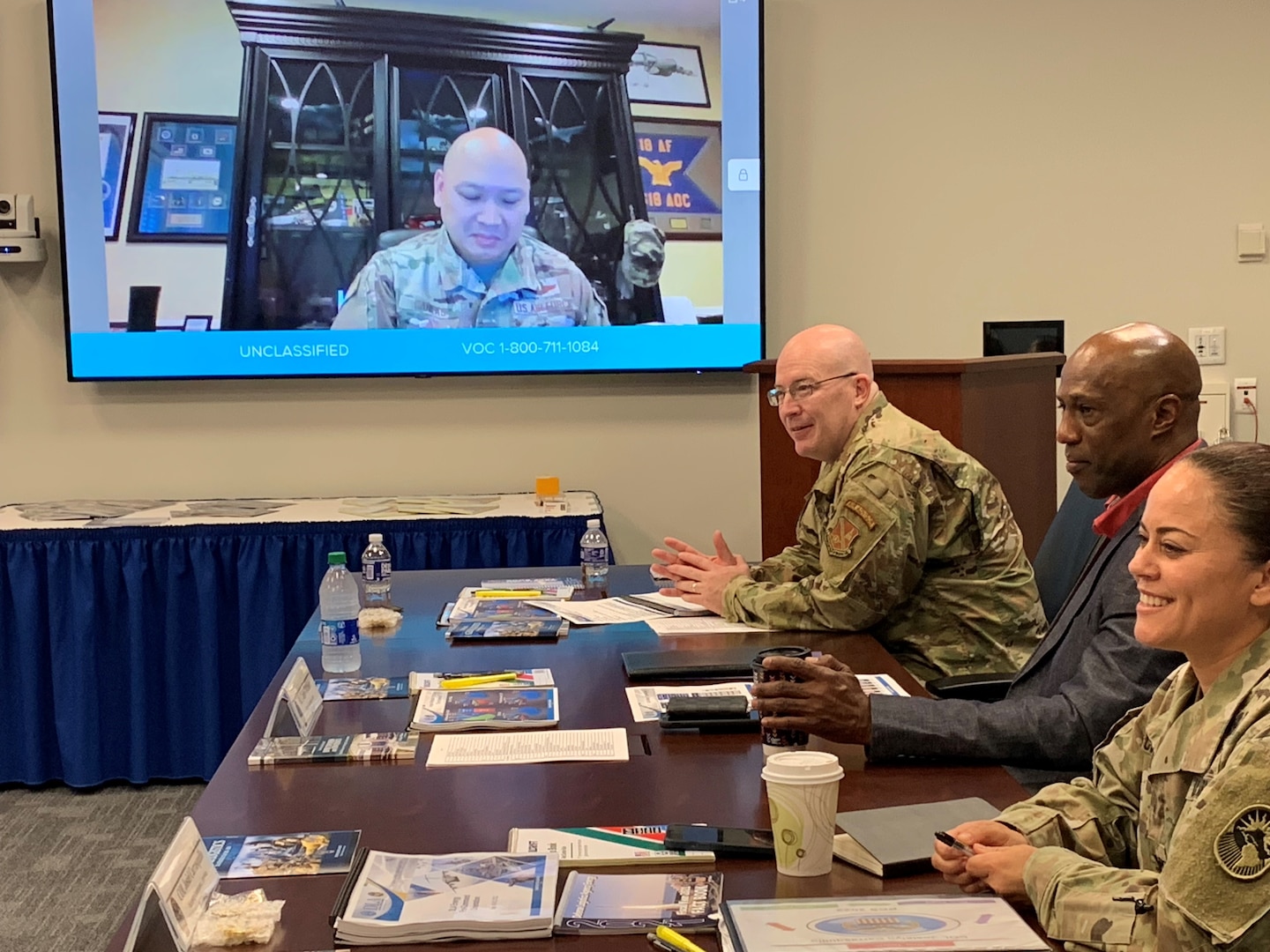 Three people sitting at a table watching a virtual presentation