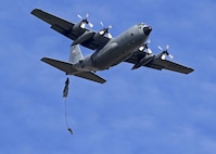 Parachute dangles from back of a plane in air.