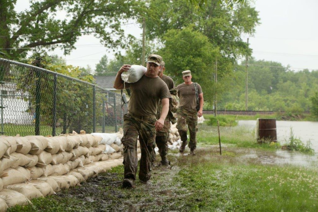 Soldiers carry sandbags.