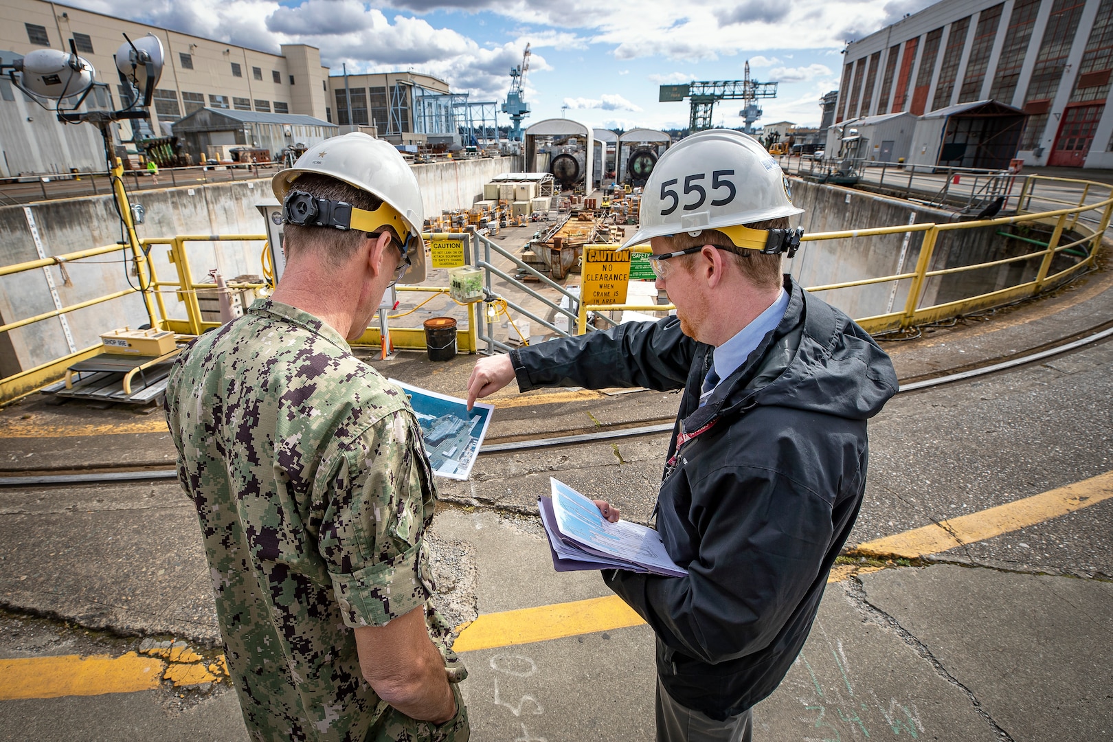 Rear Adm. Scott M. Brown, deputy commander, Naval Sea Systems Command Industrial Operations, is briefed on Shipyard Infrastructure Optimization Program by Dave Sweet, deputy program manager, PMS 555, March 31, 2022 during a tour of Puget Sound Naval Shipyard & Intermediate Maintenance Facility. Brown is the Waterfront Pillar lead for Naval Sustainment System-Shipyard, one of nine pillars meant to support the mechanics at the deckplate level and empower them to innovate and elevate issues. (U.S. Navy photo by Scott Hansen)