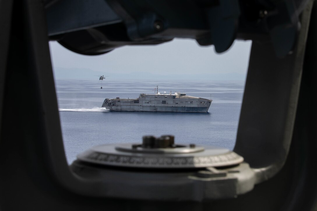 A ship is seen from an opening in a helicopter.