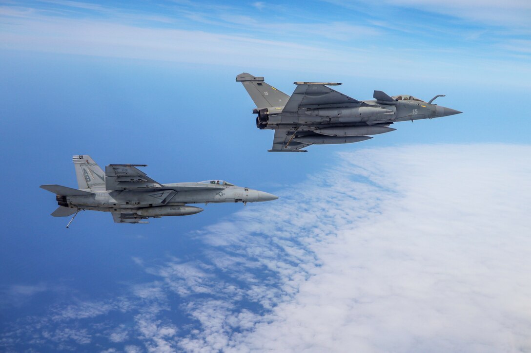 Two military jets fly alongside one another.