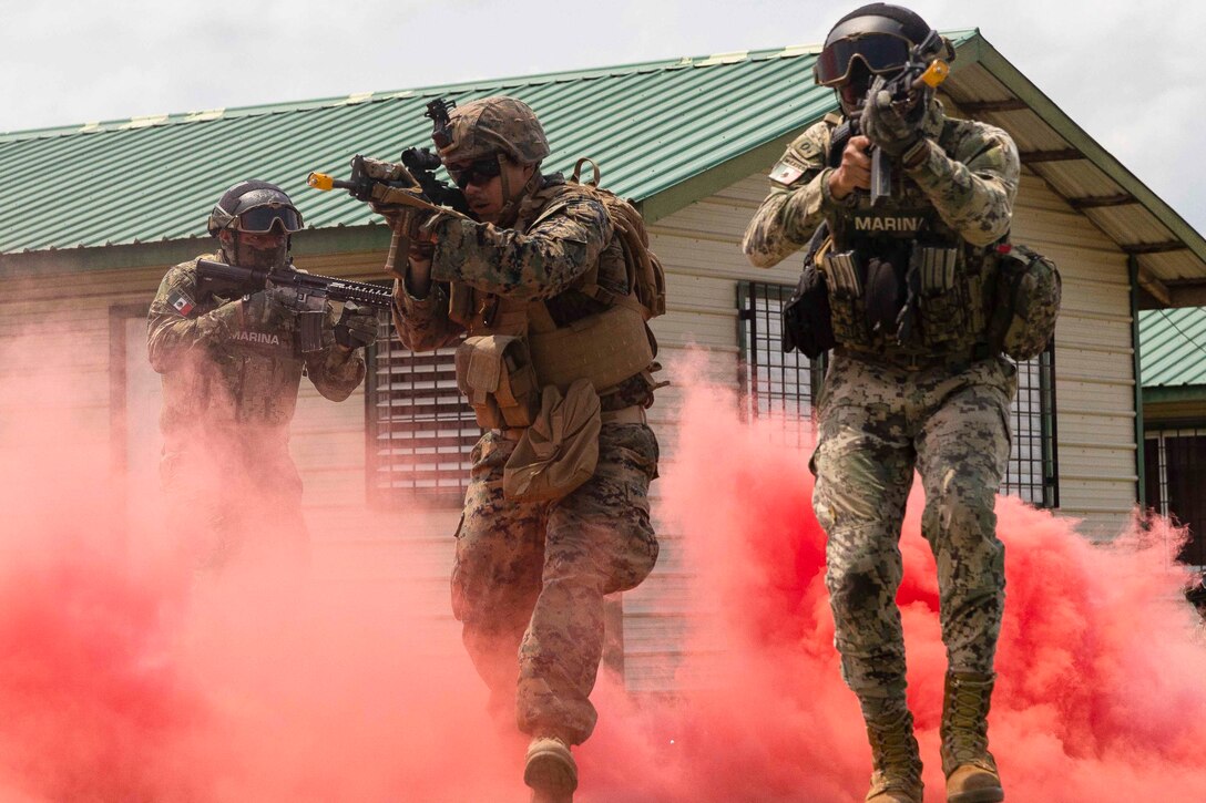 Marines move through a cloud of red smoke while holding weapons.