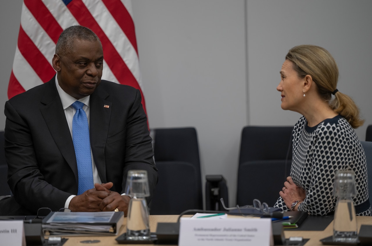 A man and a woman sit at a table and speak to one another.