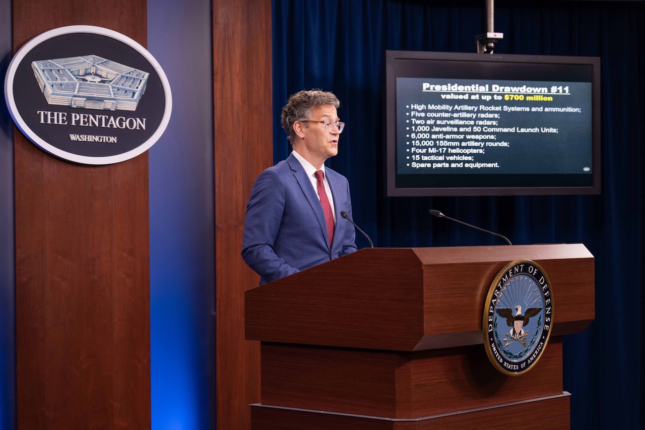 Colin Kahl, undersecretary of defense for policy, stands at a podium with a monitor on the side.