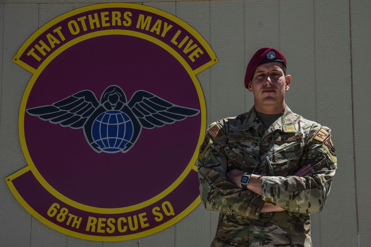 A photo of an Airman posing for a photo in front of a unit symbol.