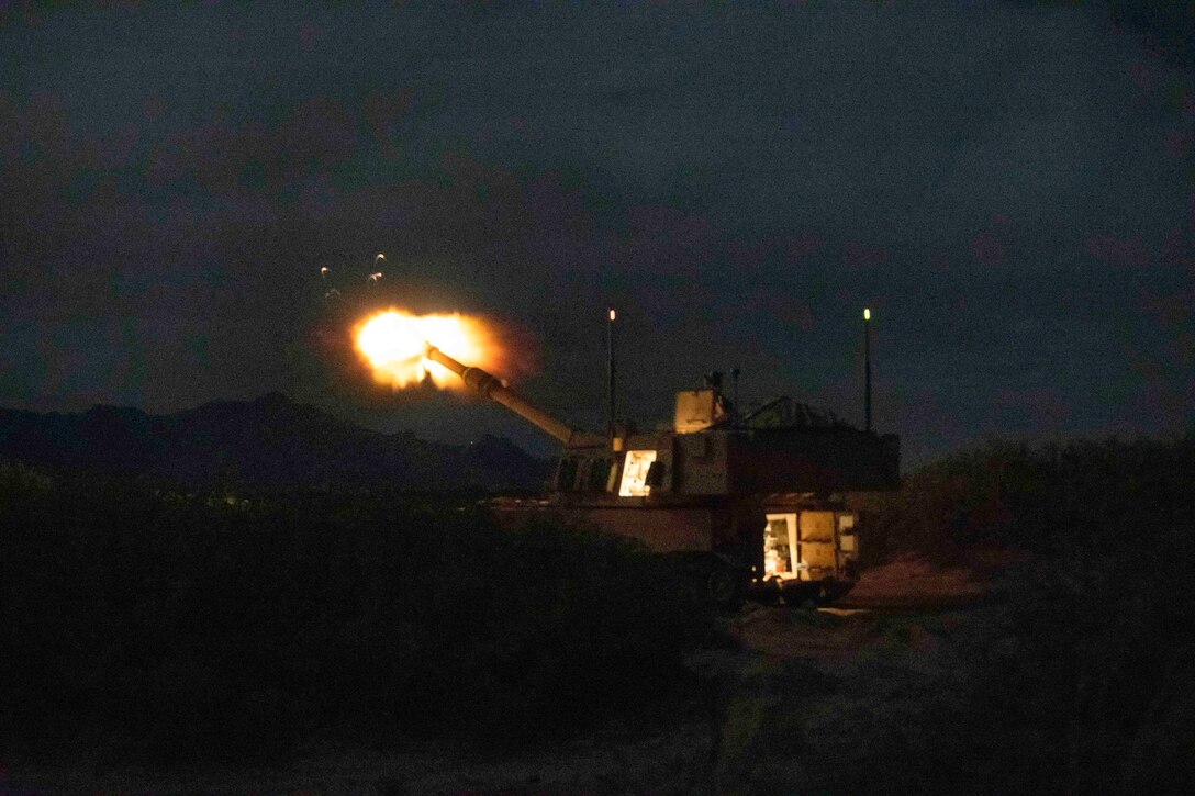 A howitzer fires in a field in the dark.