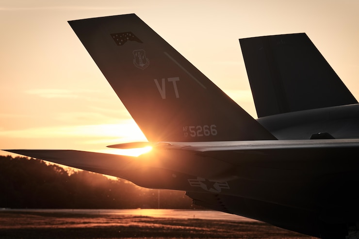 Photo of the Tail of an F-35 in the foreground of a sunset.