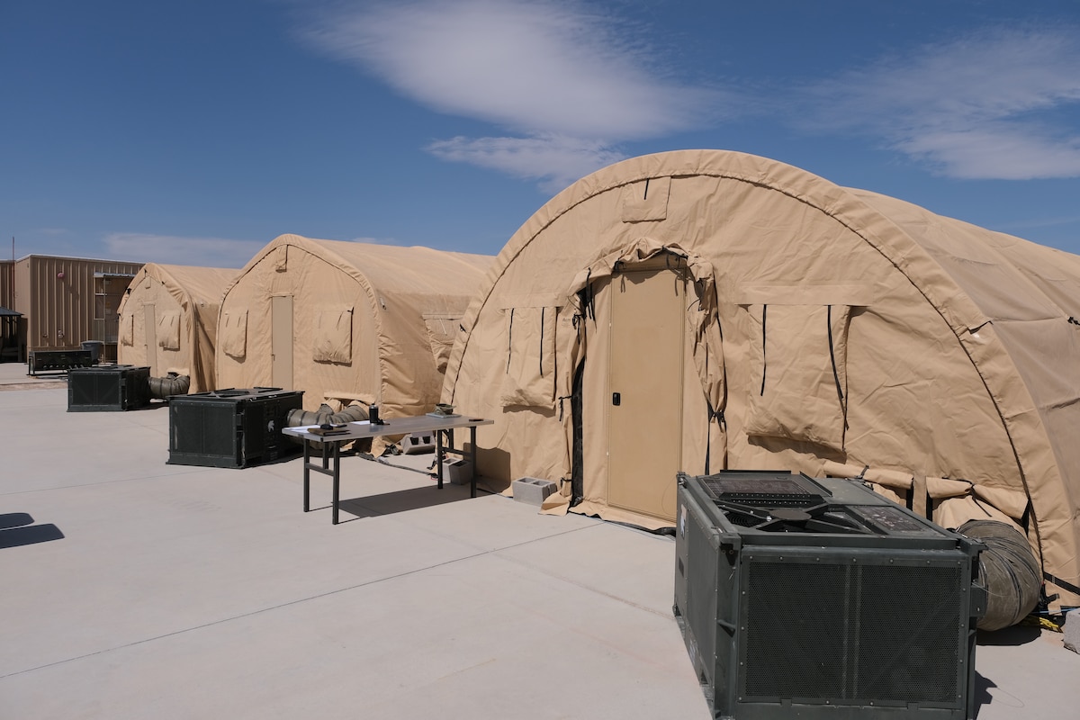 photo of three tan tents side-by-side with military equipment and a table near the tents.