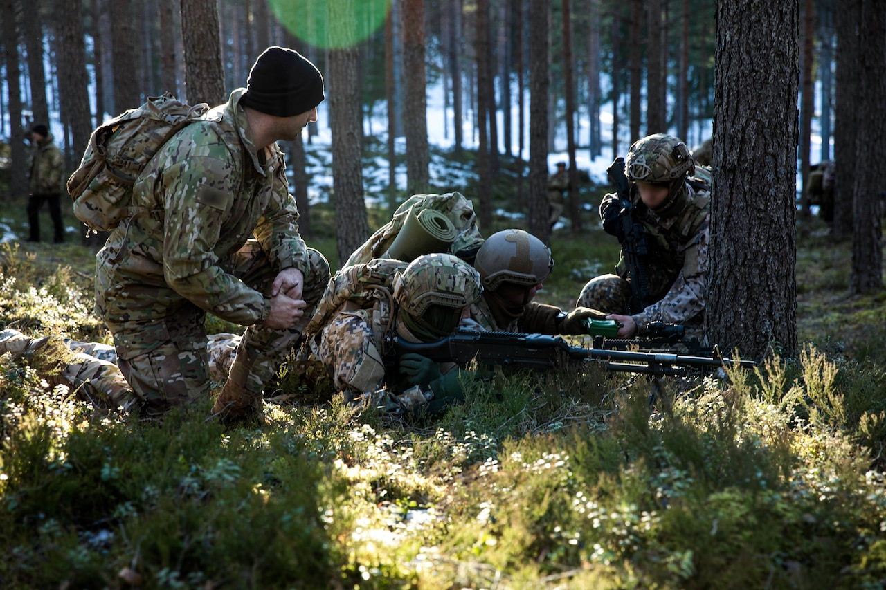 Soldier watches as other soldiers disarm a mine.