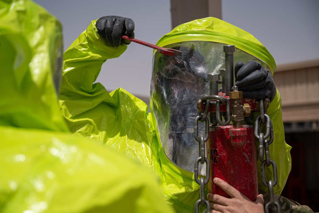 An airman wearing protective gear tightens bolts on a container.