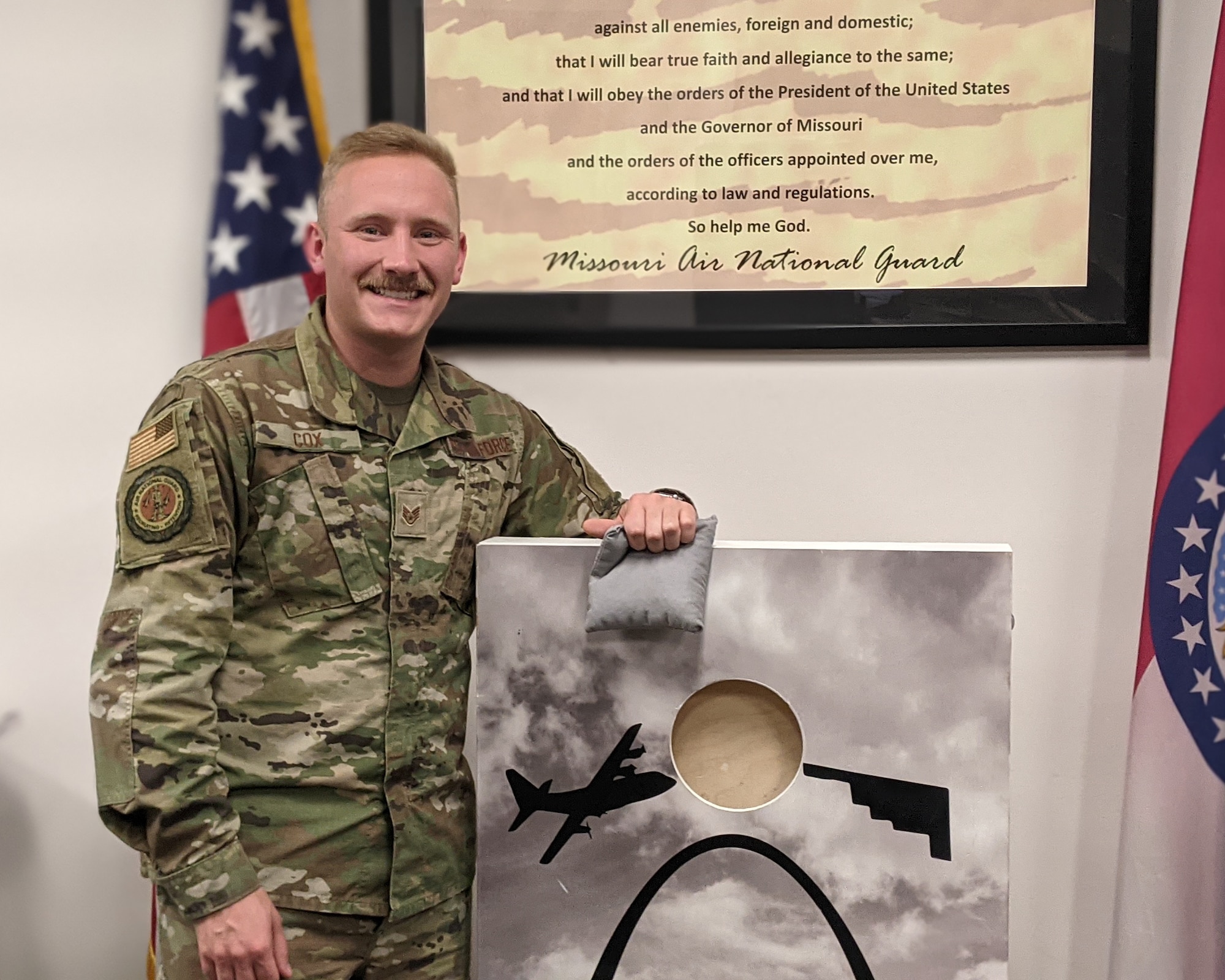 Staff Sgt. Johnny Cox is a recruiter with the 131st Bomb Wing, Missouri Air National Guard, as well as a professional cornhole player. Whether it's on base, in the community, or on the court, Cox represents the integrity, service and excellence of Missouri's Airmen.
An Airman in OCP uniform shows off a cornhole board with aircraft graphics.