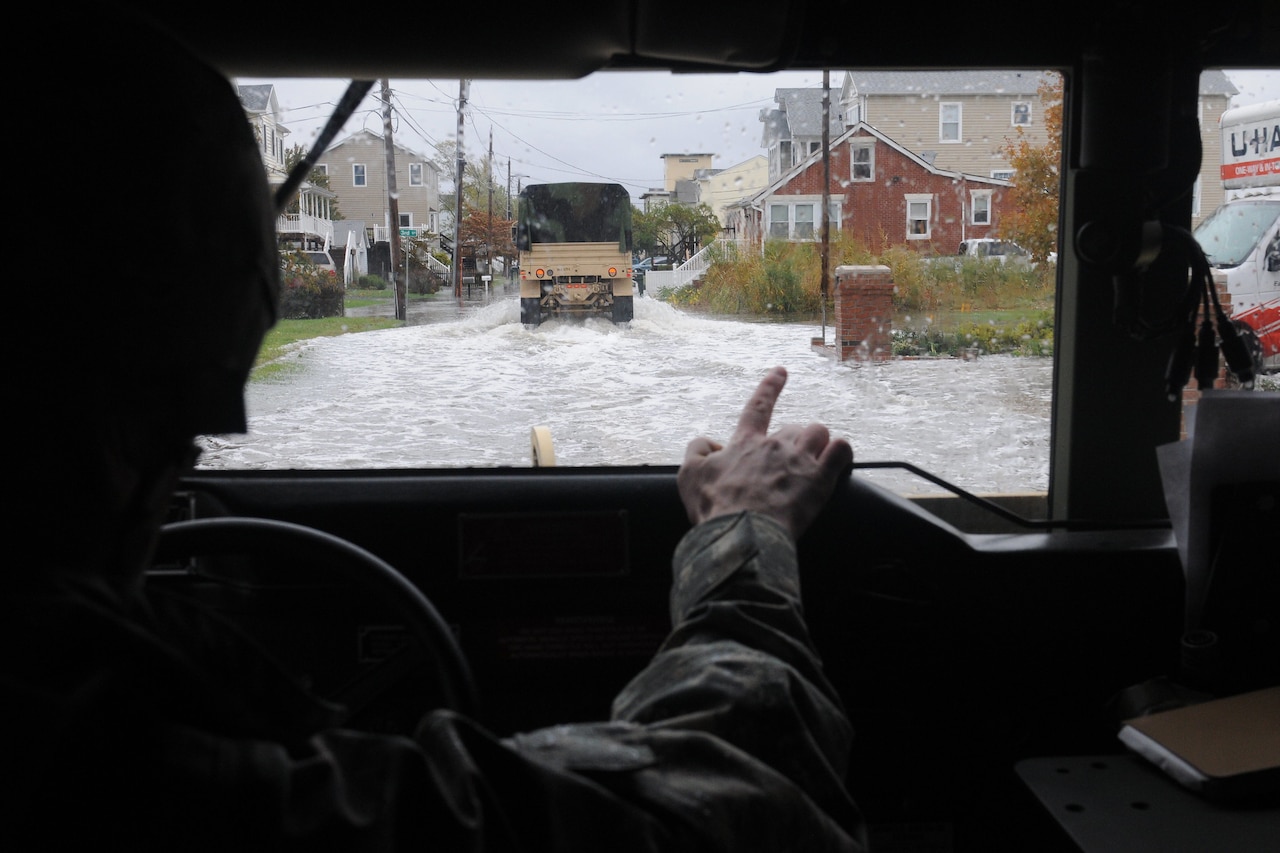 A driver points out a window as they drive through flooded streets.