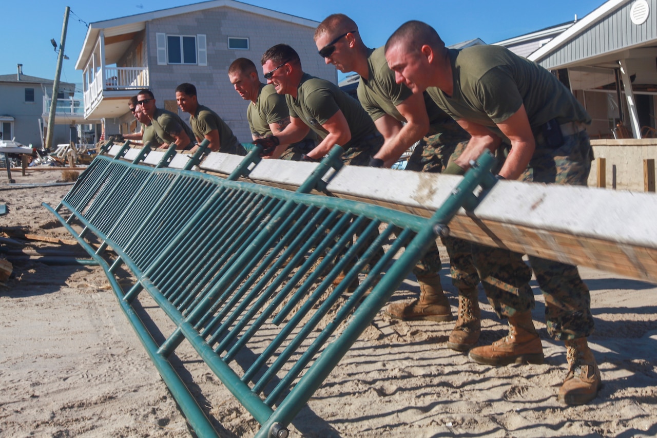 Several men bend over to lift a medal fence on a beach.