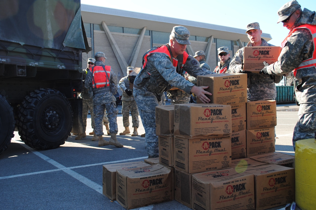 Men pile boxes of emergency meals on the ground near a truck.