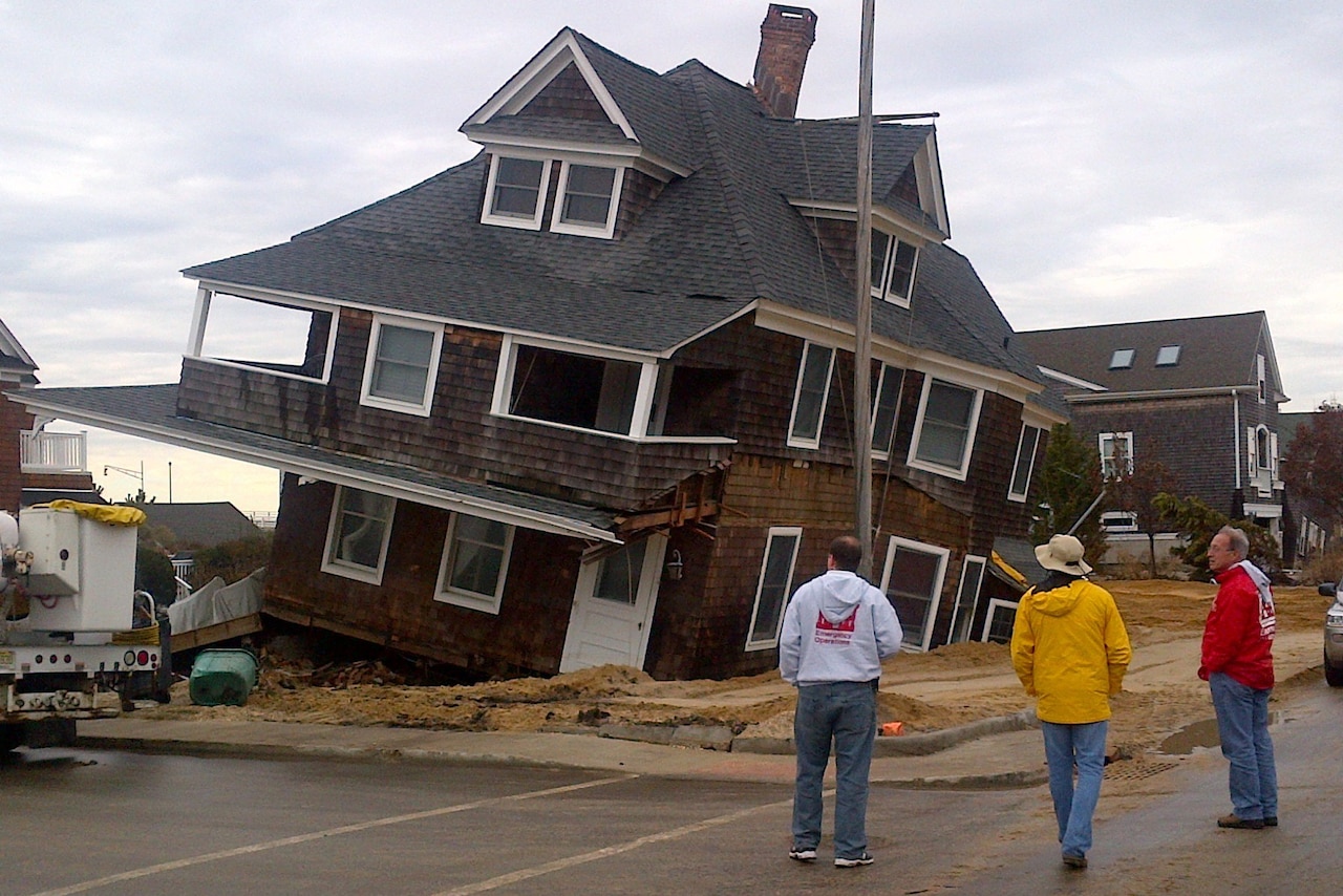 Three men look at a sinking, crooked house.