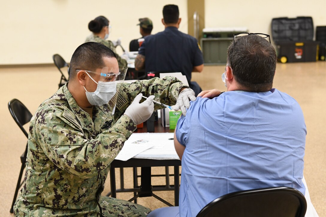 A man injects a shot into another man’s arm.