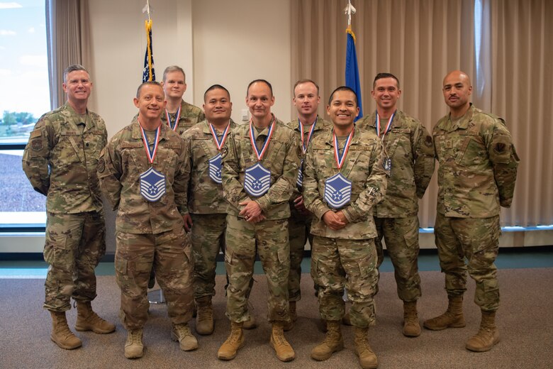 Master sergeant selects pose with Lt. Col. Benjamin Hughes, 460th Healthcare Operations Squadron commander, (far left) and Senior Master Sgt. Archie Curtis, senior enlisted leader of the 566th Intelligence Squadron, (far right) following the closing of their promotion release ceremony.