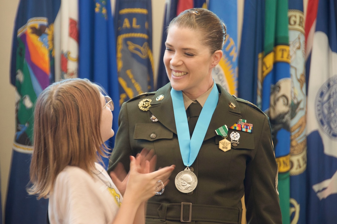 A soldier wearing a medal smiles at her daughter during a ceremony.