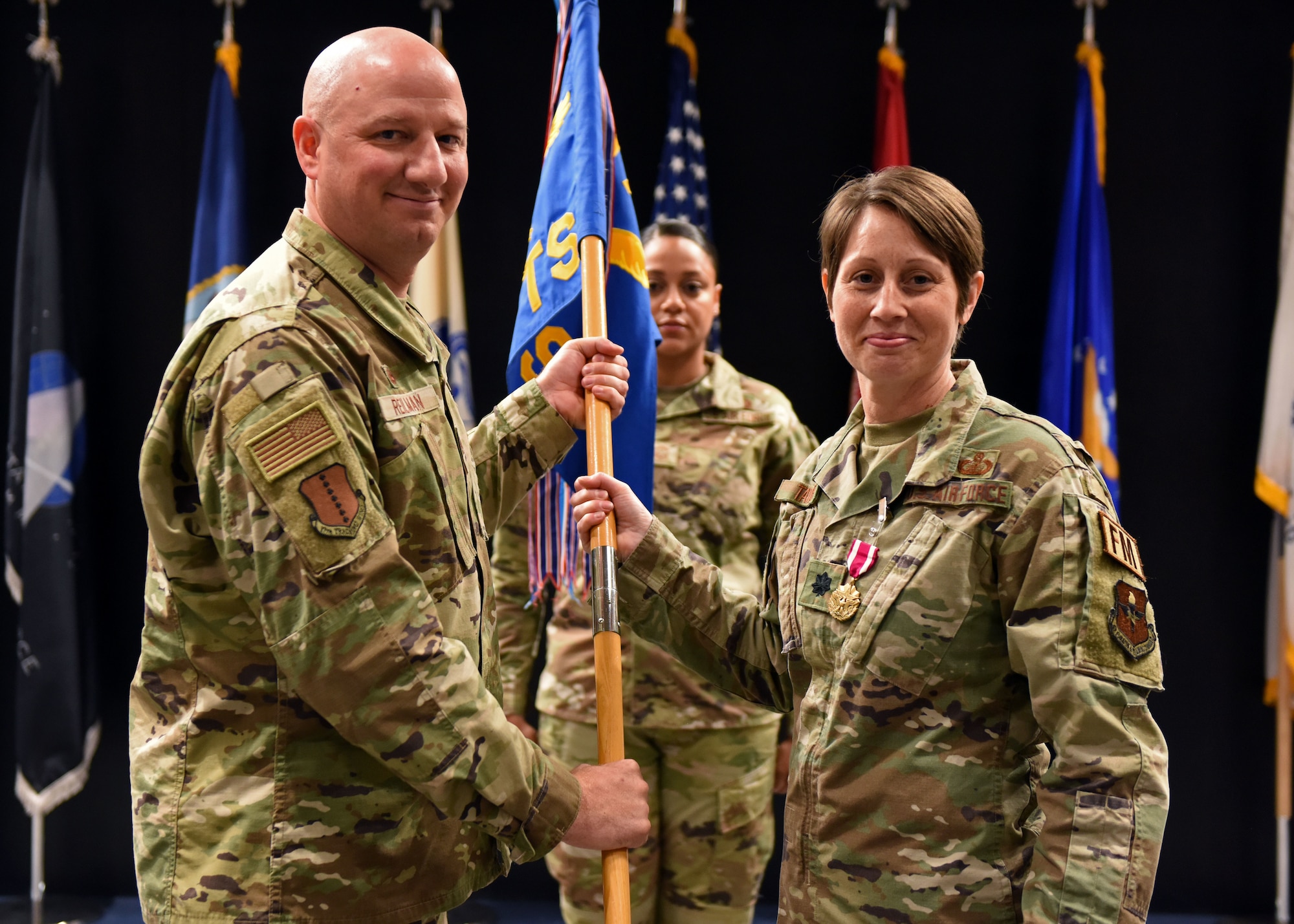 U.S. Air Force Lt. Col. Kara Taylor, 17th Comptroller Squadron outgoing commander, (right) relinquishes command to Col. Matthew Reilman, 17th Training Wing commander, during the 17th CPTS change of command ceremony at the Powell Event Center, June 3, 2022. Passing the guidon physically represents the symbolism of passing the squadron responsibilities to the next commander. (U.S. Air Force photo by Airman 1st Class Sarah Williams)