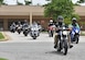 Motorcycle riders drive together in a side by side formation down the street.