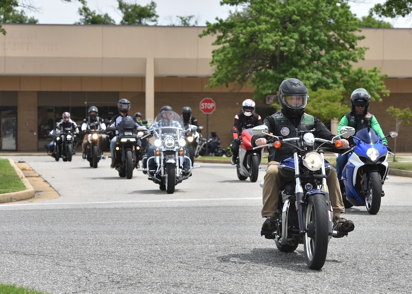 Motorcycle riders drive together in a side by side formation down the street.