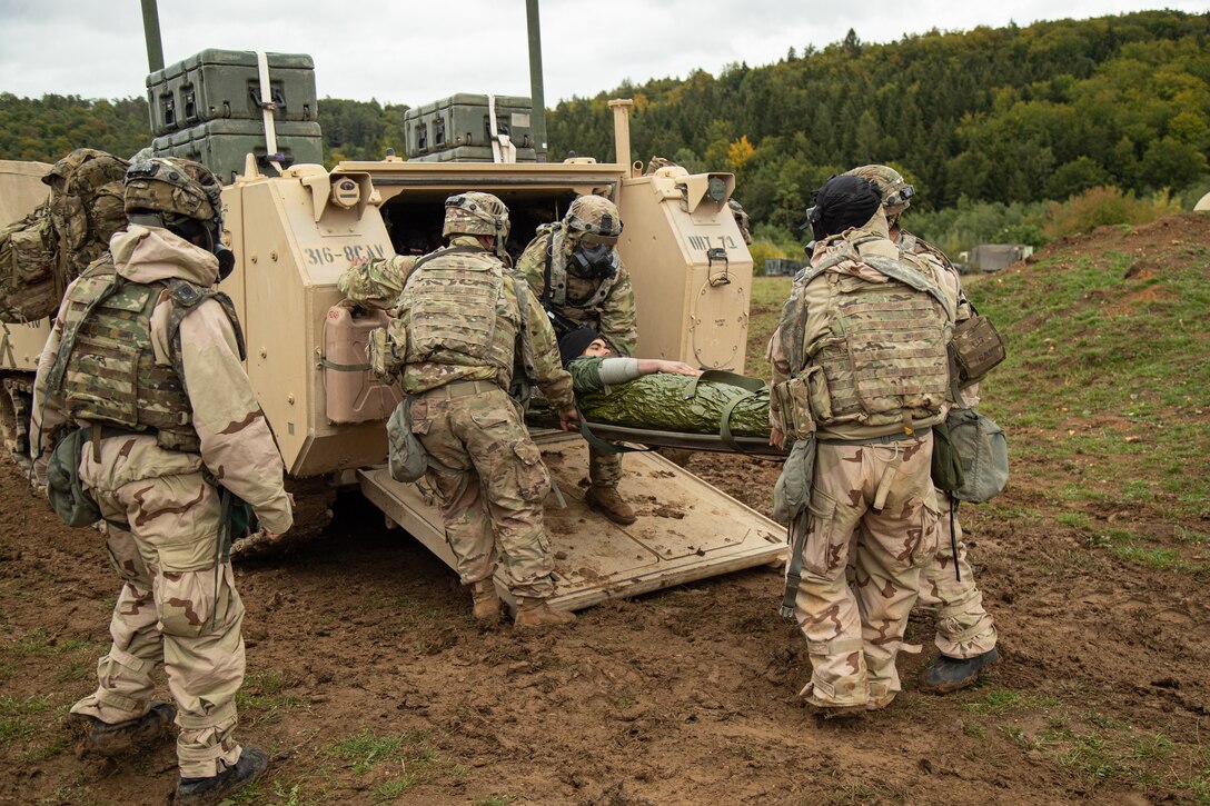 Soldiers use a stretcher to remove a person from the rear of a combat vehicle.