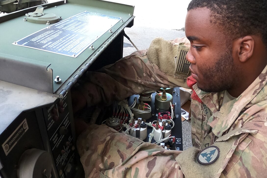 A service member reaches into an open panel on a piece of mechanical equipment.