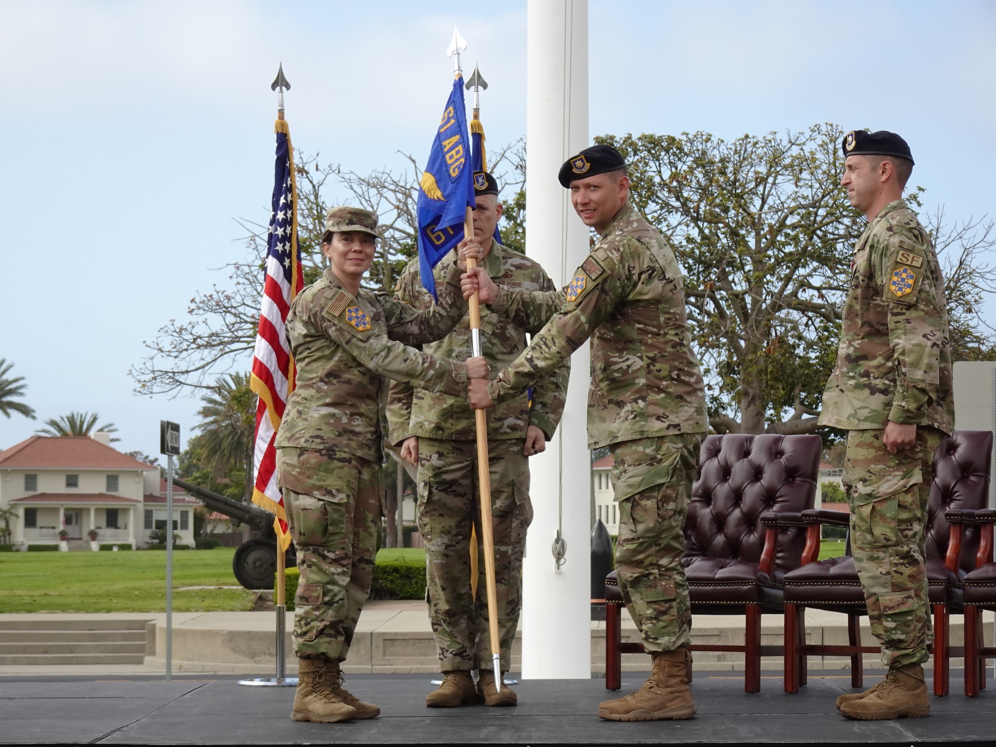 Col. Becky Beers, Los Angeles Garrison commander, left, turns over the 61st SFS command guidon to Maj. Brandon Burden, new 61st SFS commander, right at his change of command ceremony which was held June 1 at Fort MacArthur. Chief Master Sgt. Michael Groder, 61st SFS senior enlisted leader, stands ready to post the gideon.  Maj Burden’s unit will secure four bases, the $10 billion Space Systems Command acquisition mission and more than 600 families.