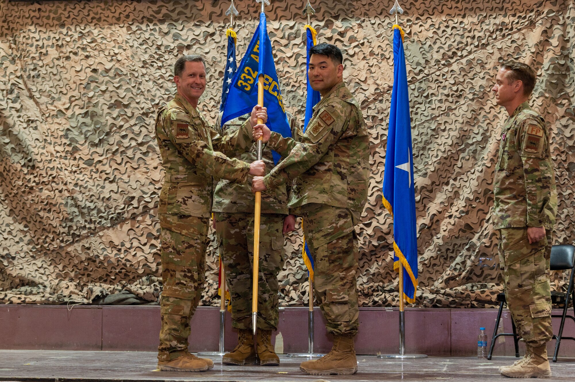 U.S. Air Force Brig. Gen. Christopher Sage, 332d Air Expeditionary Wing commander, exchanges the 332d Expeditionary Civil Engineer Squadron guidon with U.S. Air Force Lt. Col. Sean Chun, 332d ECES incoming commander, during a change of command ceremony at an undisclosed location in Southwest Asia, June 2, 2022. A change of command ceremony is a tradition that represents a formal transfer of authority and responsibility from the outgoing commander to the incoming commander. The 332d ECES provides, operates, and maintains a sustainable installation through engineering and emergency response services across the full mission spectrum. (U.S. Air Force photo by Tech. Sgt. Lauren M. Snyder)