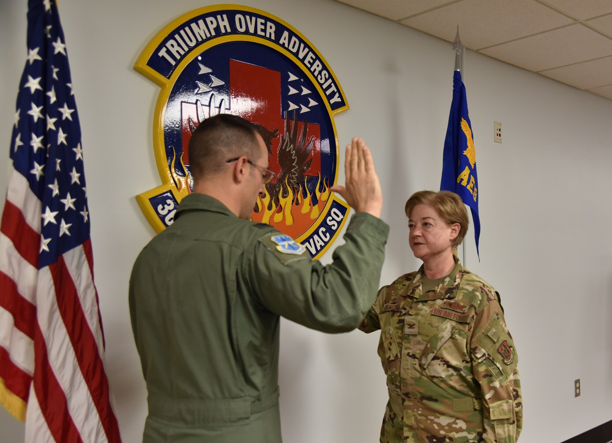 Col. Kevin Campanile on right side stands with his right hand raised to swear in Col. Ladonna Schreffler, on left side, for her promotion to colonel.