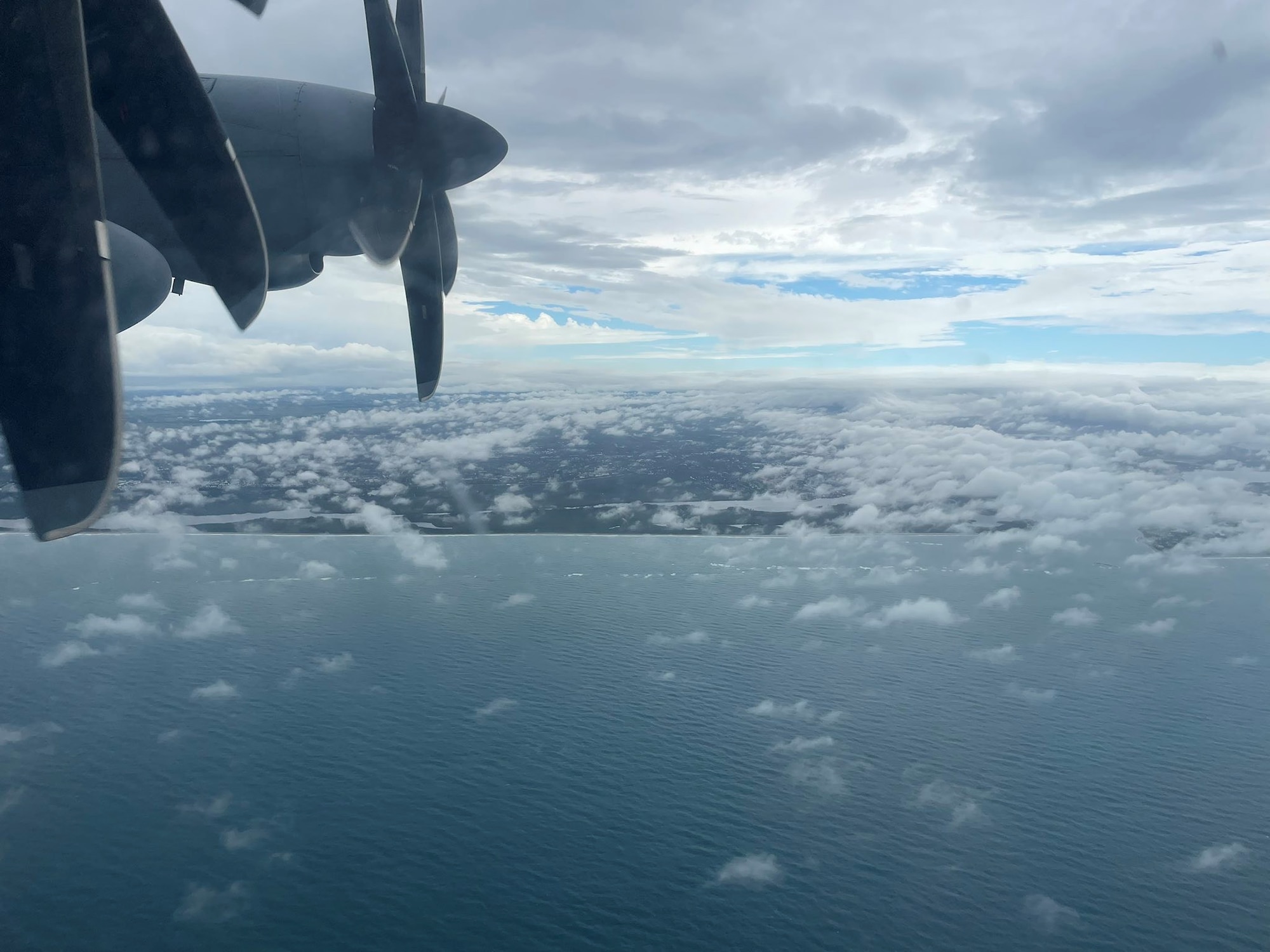 Two WC-130J engines can be seen with ocean, clouds and land in the background.