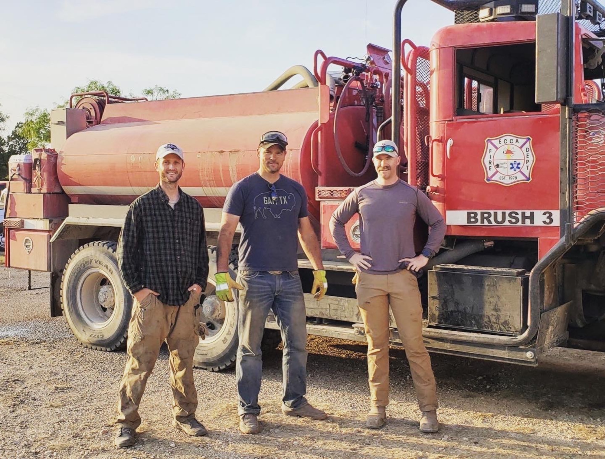 Three men stand in front of an emergency response vehicle.