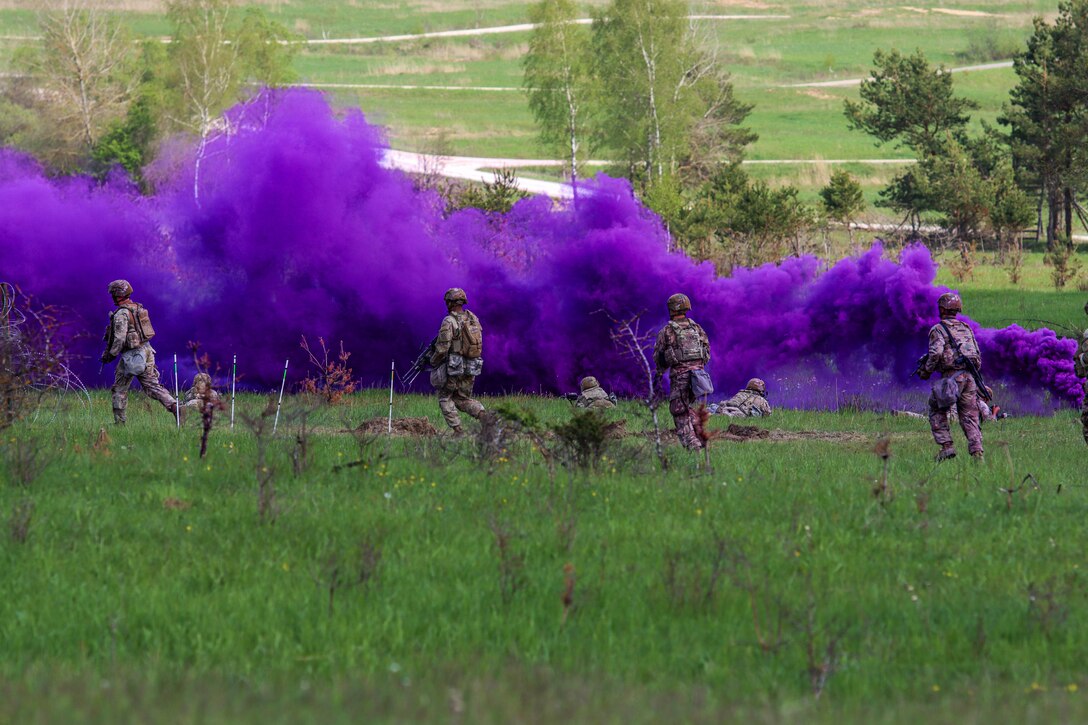 Soldiers are in a field behind the cover of purple smoke.