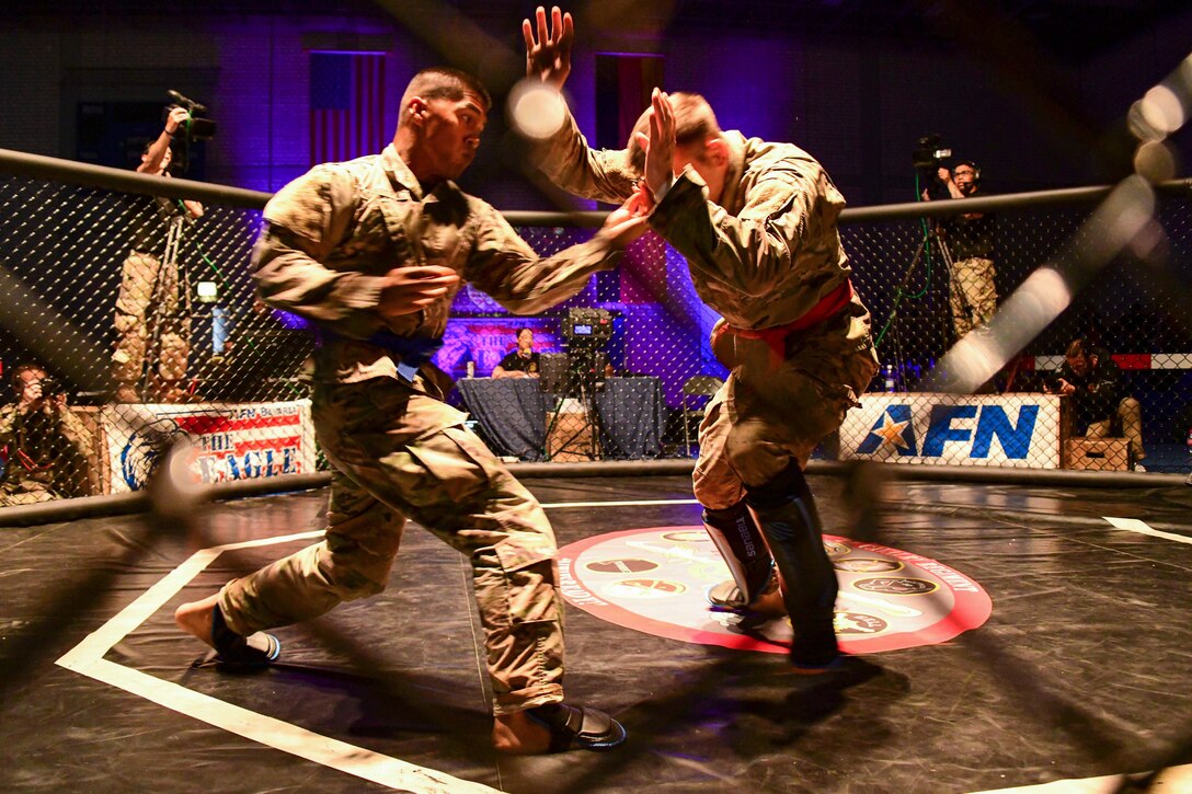 Two soldiers fight in a ring during training as camera crews film.