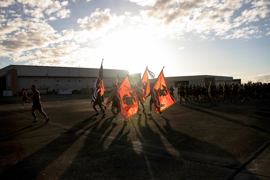 A group of sailors and Marines run at twilight.