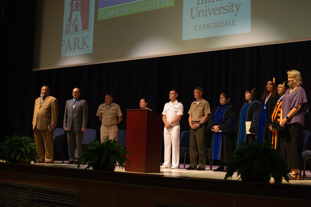 Distinguished guest stand on stage during the processional at the 46th Annual Voluntary Education Graduation Ceremony at Two Rivers Theater, MCAS Cherry Point, North Carolina, June 2, 2022. The goals of the voluntary education programs are to provide a broad range of personal and professional learning opportunities to improve the academic abilities of active-duty personnel to assist in their career progression and to generally strengthen the military community. (U.S. Marine Corps photo by Lance Cpl. Symira Bostic)